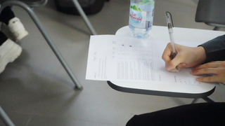 Élève écrit sur bulletin avec stylo sur tablette-bureau en salle de classe.