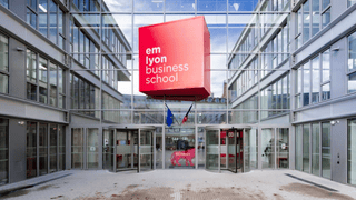 Entrée em lyon business school : cube rouge suspendu, façade vitrée et portes tournantes.