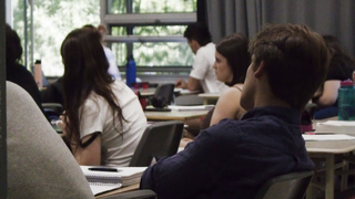 Étudiants en cours dans une salle de classe lumineuse avec bureaux, carnets et fenêtre.