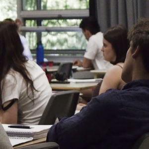 Étudiants en cours dans une salle de classe lumineuse avec bureaux, carnets et fenêtre.