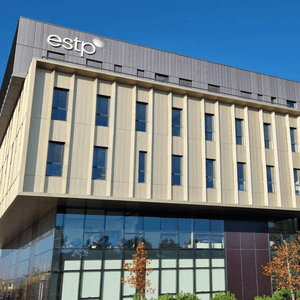 Bâtiment contemporain ESTP en verre et métal, façade surplombante, fenêtres verticales, ciel bleu.