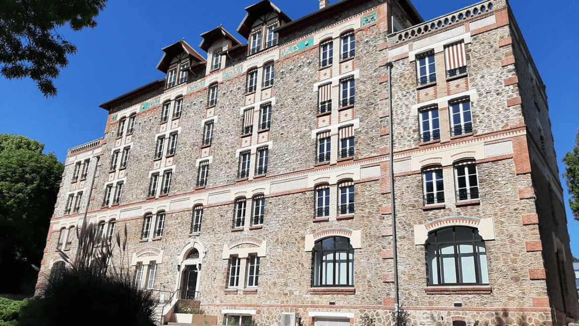 Façade en pierre dimmeuble historique au soleil, fenêtres et stores rayés.