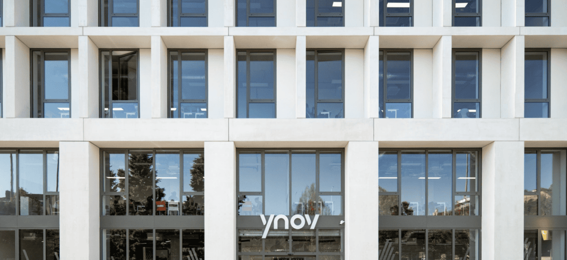 Façade moderne en béton et verre d’un bâtiment de bureaux Ynov, fenêtres modulaires reflétantes.
