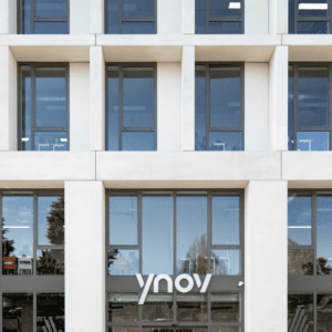 Façade moderne en béton et verre d’un bâtiment de bureaux Ynov, fenêtres modulaires reflétantes.