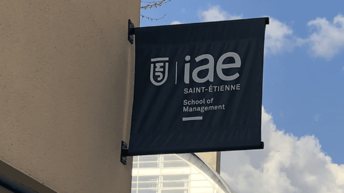Bannière IAE Saint-Étienne, école de management sur façade, logo visible, ciel bleu.