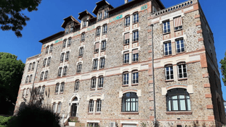 Façade en pierre dimmeuble historique au soleil, fenêtres et stores rayés.