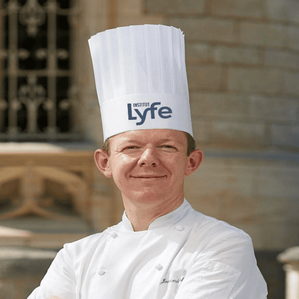 Chef professionnel en extérieur, portrait institut avec toque Lyfe et veste blanche.