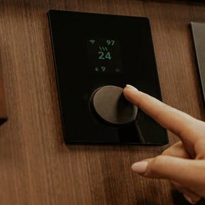Thermostat mural domotique encastré dans bois, molette tactile et affichage 24°C.