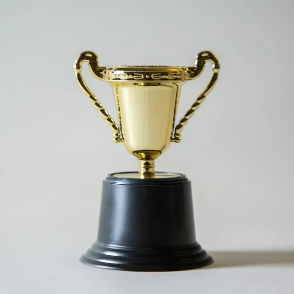 Petit trophée doré sur socle noir, coupe à deux anses, symbole de récompense.
