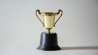 Petit trophée doré sur socle noir, coupe à deux anses, symbole de récompense.
