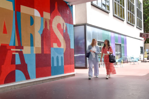Fresque colorée devant ESSCA Paris, deux étudiantes marchant près dun bâtiment moderne.