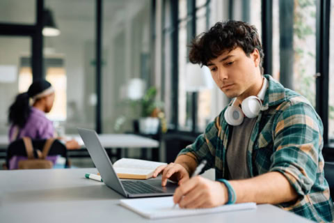 Étudiant universitaire concentré utilisant un portable et prenant des notes en salle détude.