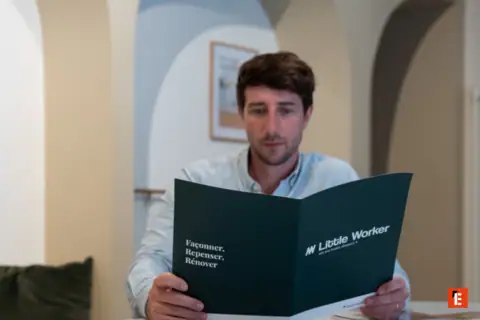 Homme lisant brochure Little Worker, franchise rénovation dans intérieur chaleureux.